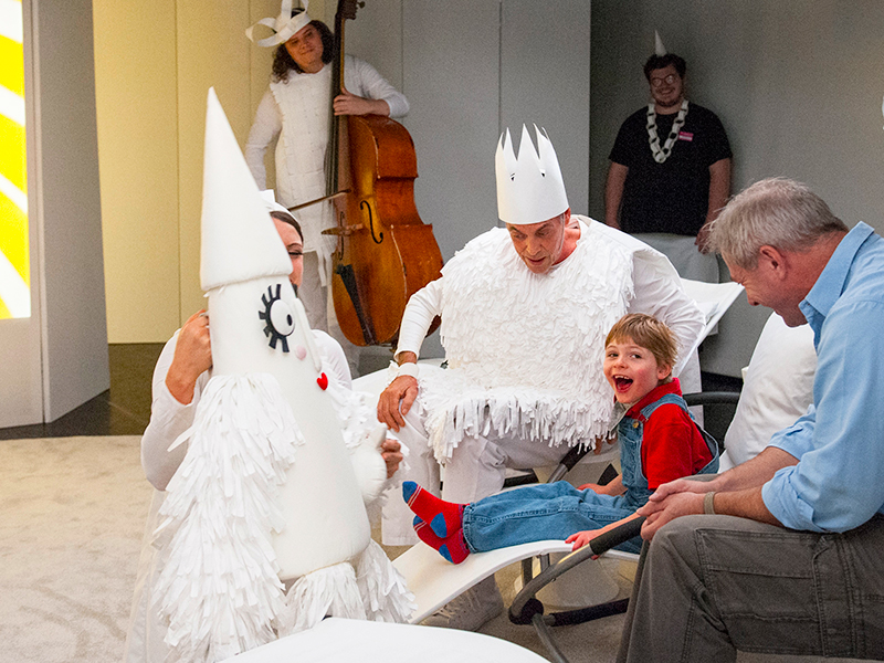 A young boy interacts with characters dressed in white paper costumes.