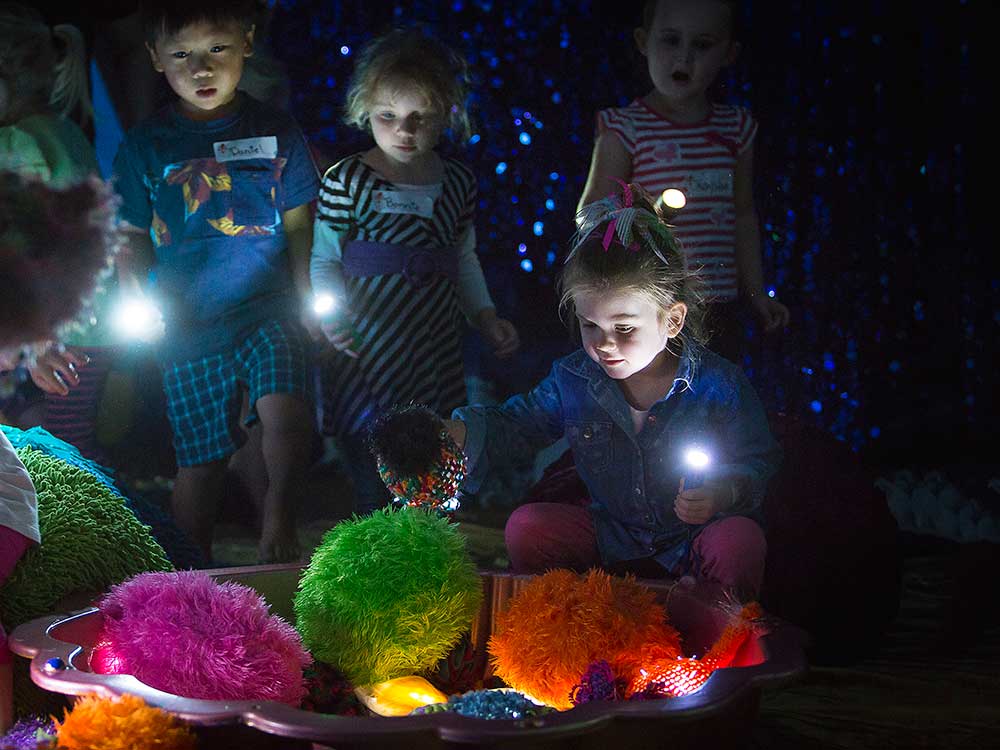 In a dark room, children explore flourescent sea-like creatures.