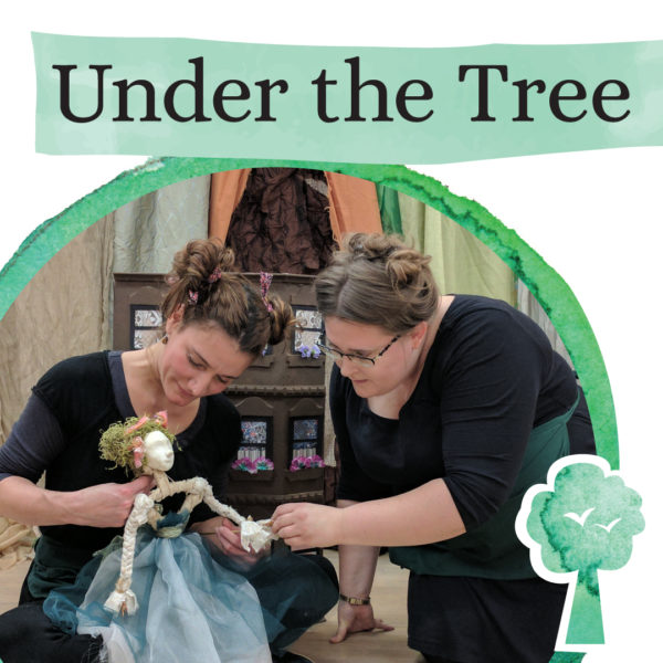 Two women dressed in black hold a doll. Their image is surrounded by a green 3/4 circle with a tree in the lower-right corner. Above the picture, black text reads "Under the Tree" on a green background.