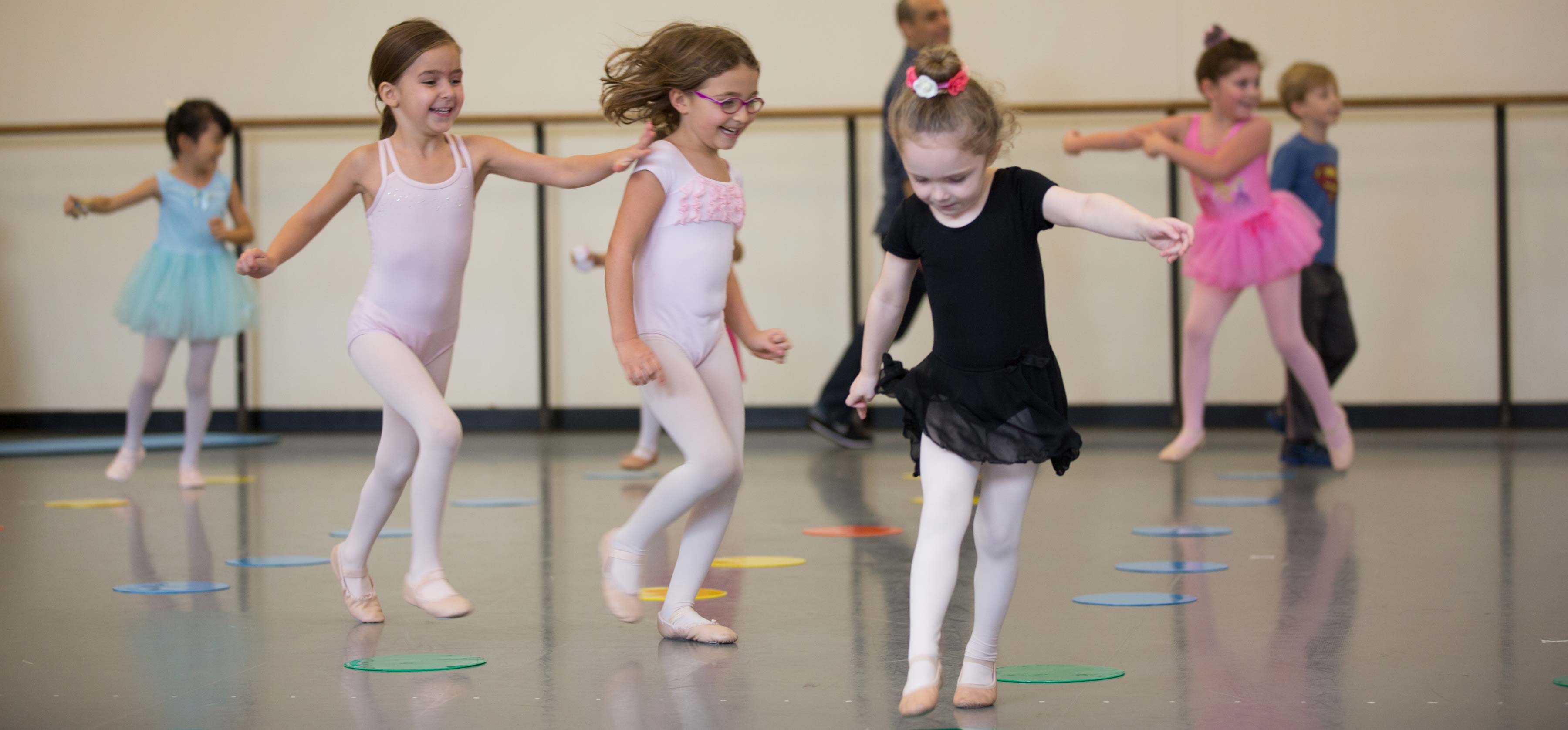 An image of several young ballet dancers in a row, practicing in a dance studio.