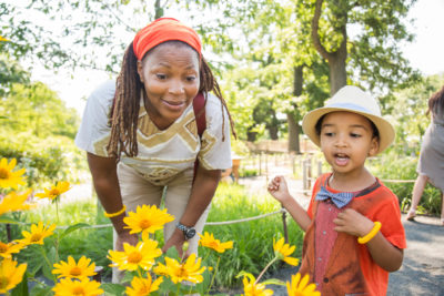 A woman and a child look at a green bush with yellow flowers