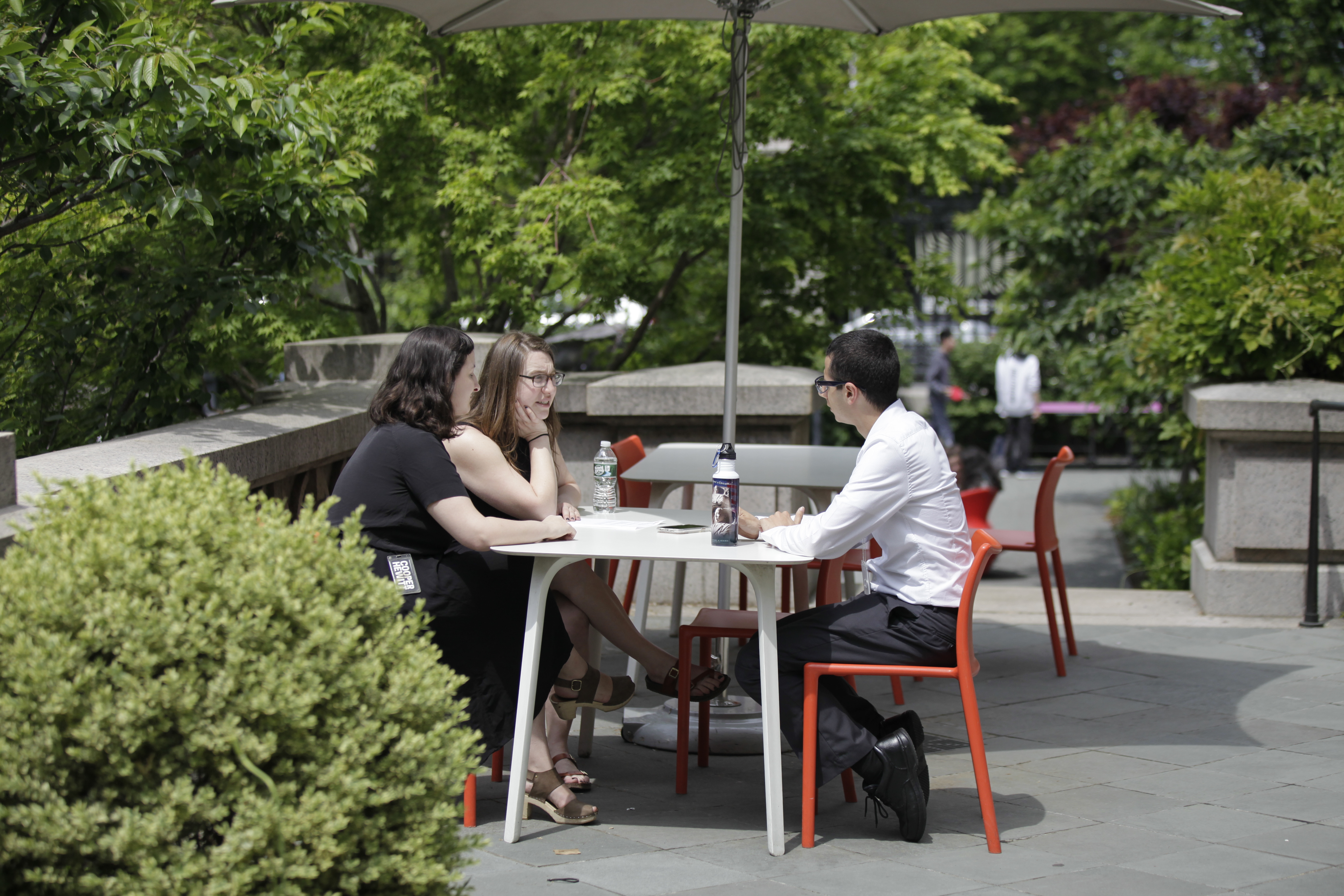 Three people sit at a table under an umbrella in the Cooper Hewitt garden