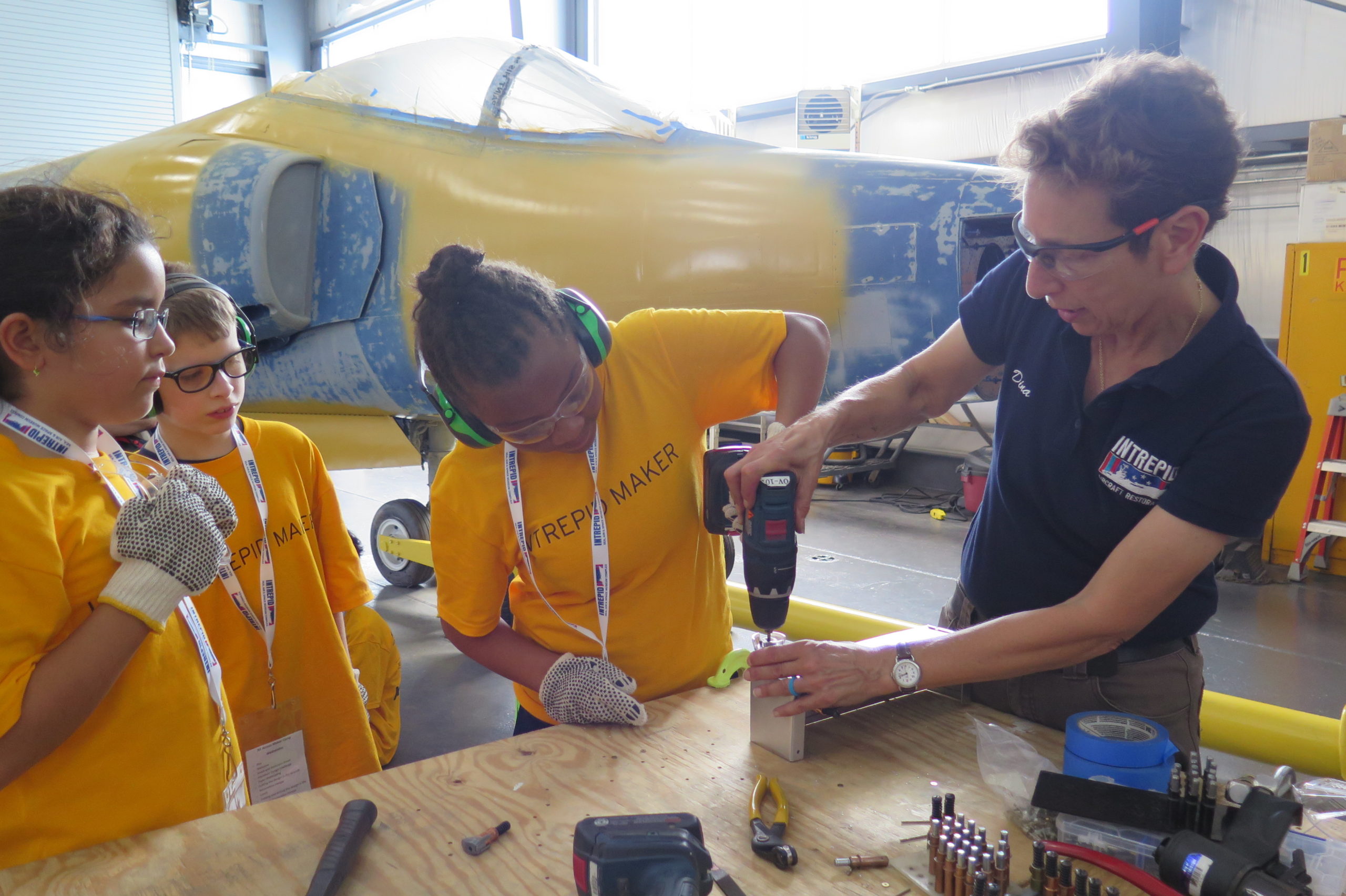 Three young people wearing headphones work with museum educator to assemble a model