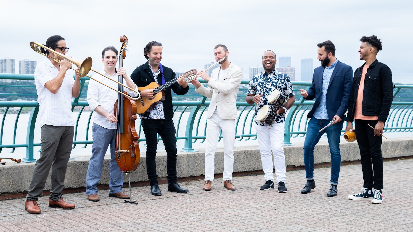 A group of musicians stands by a waterfront joyously playing their instruments.